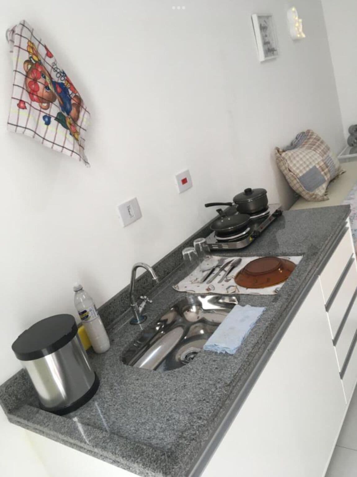 Una cocina con encimera de granito, pileta de acero inoxidable y diversos utensilios de cocina.