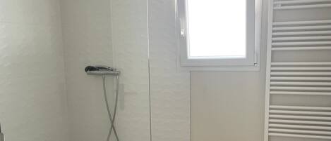 A shower room with a glass door, a window, and a towel rack.