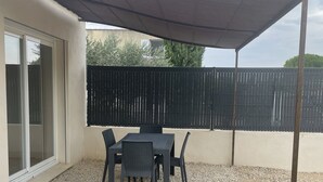 Un patio exterior con una mesa y sillas, una pérgola que da sombra y suelo de grava.