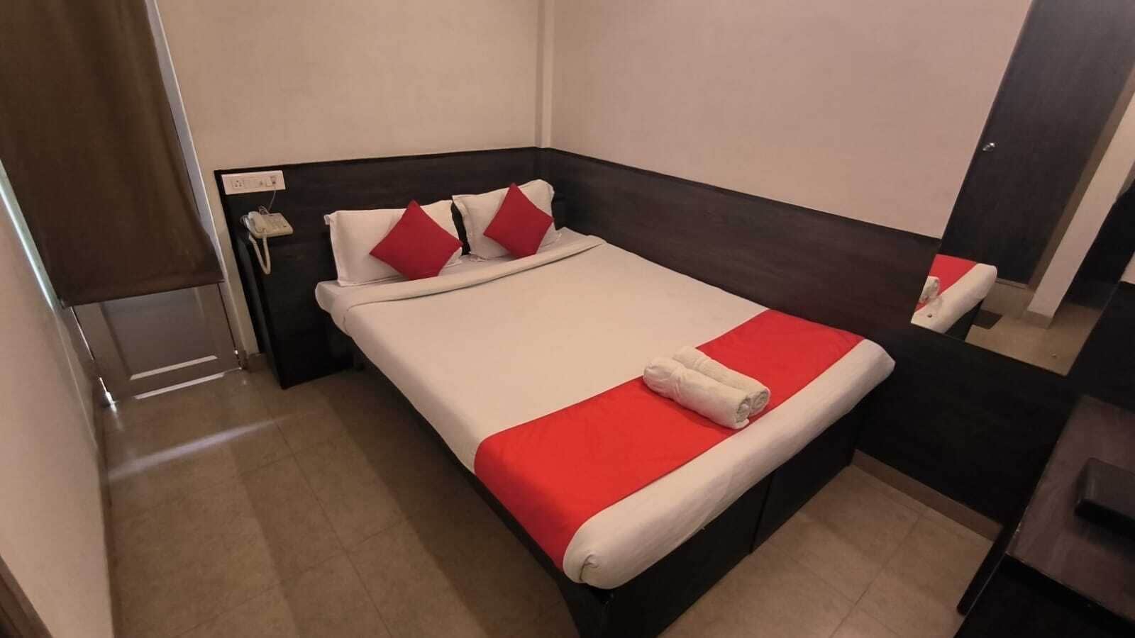 A hotel room with a bed, a nightstand, a mirror, and a door.