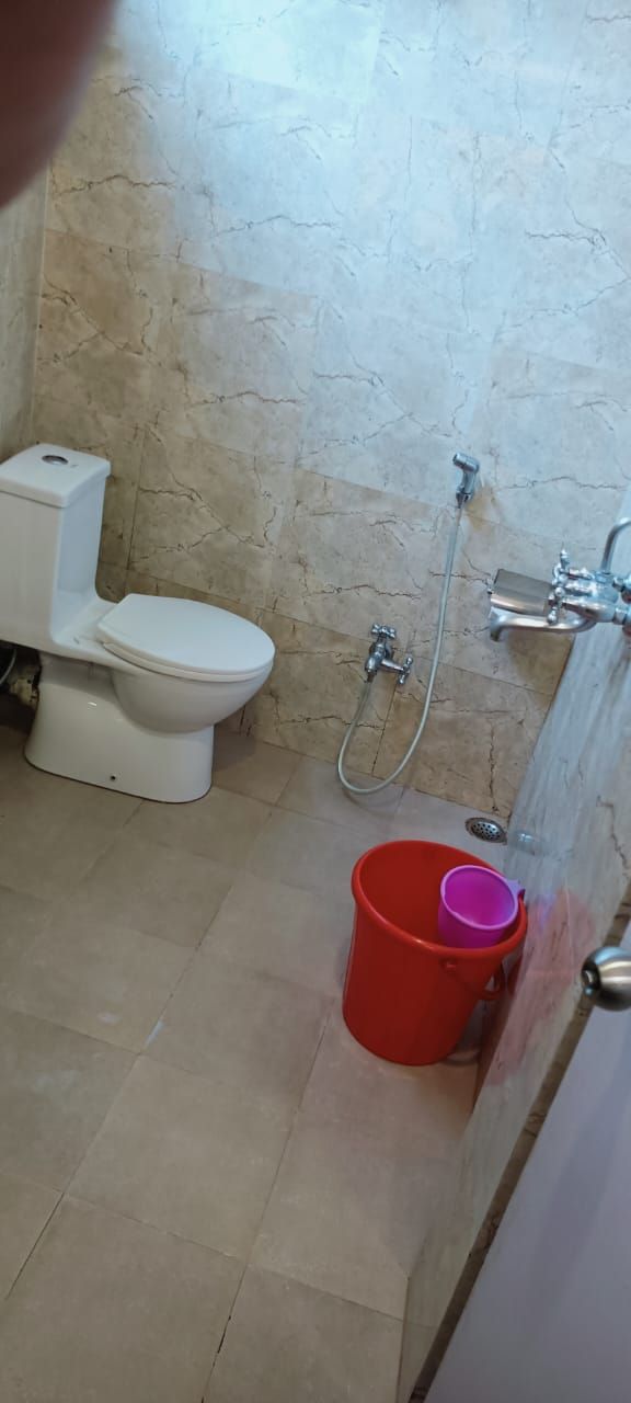 Een badkamer met toilet, douche en een rode emmer.