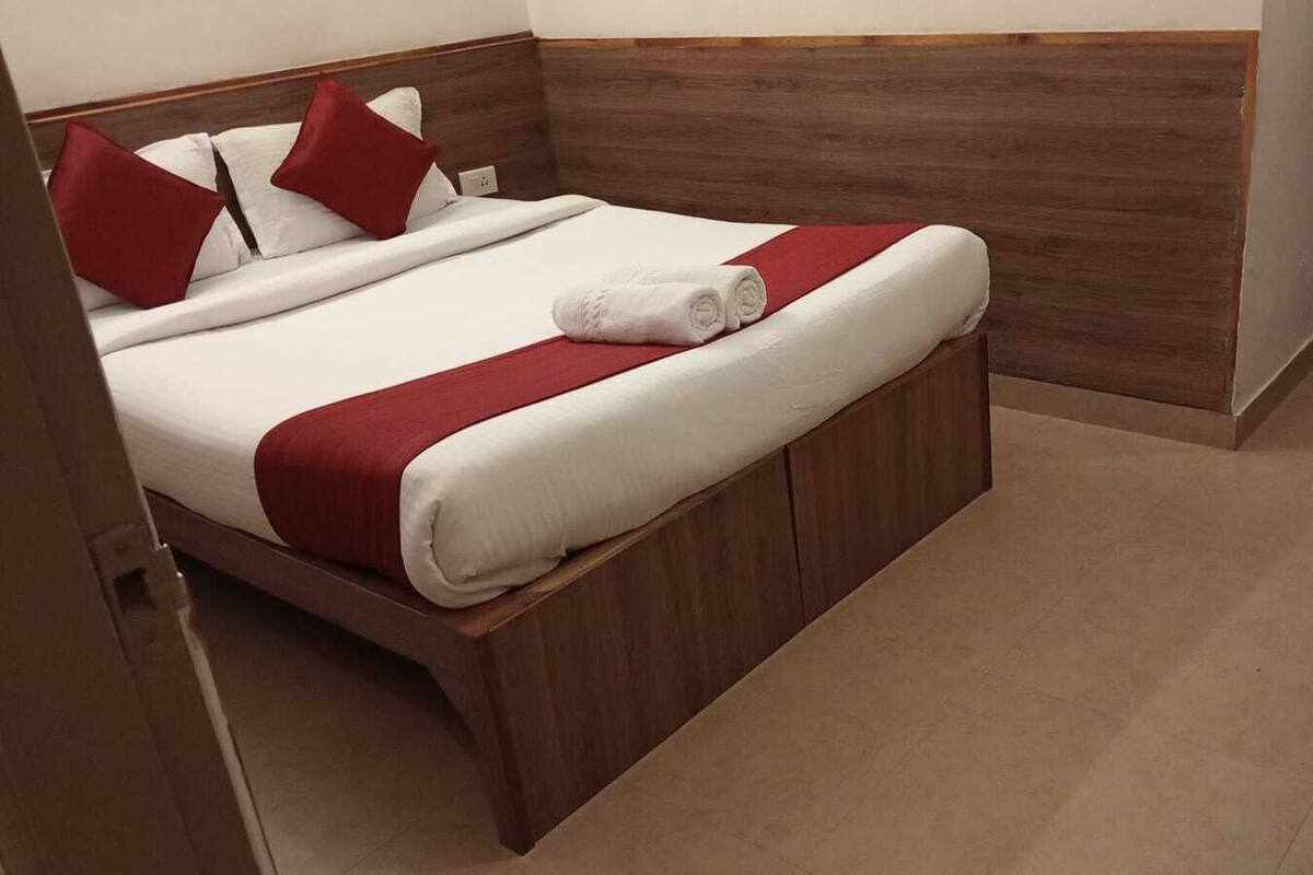 A neatly made bed with a red and white bedspread, two red pillows, and a rolled white towel.