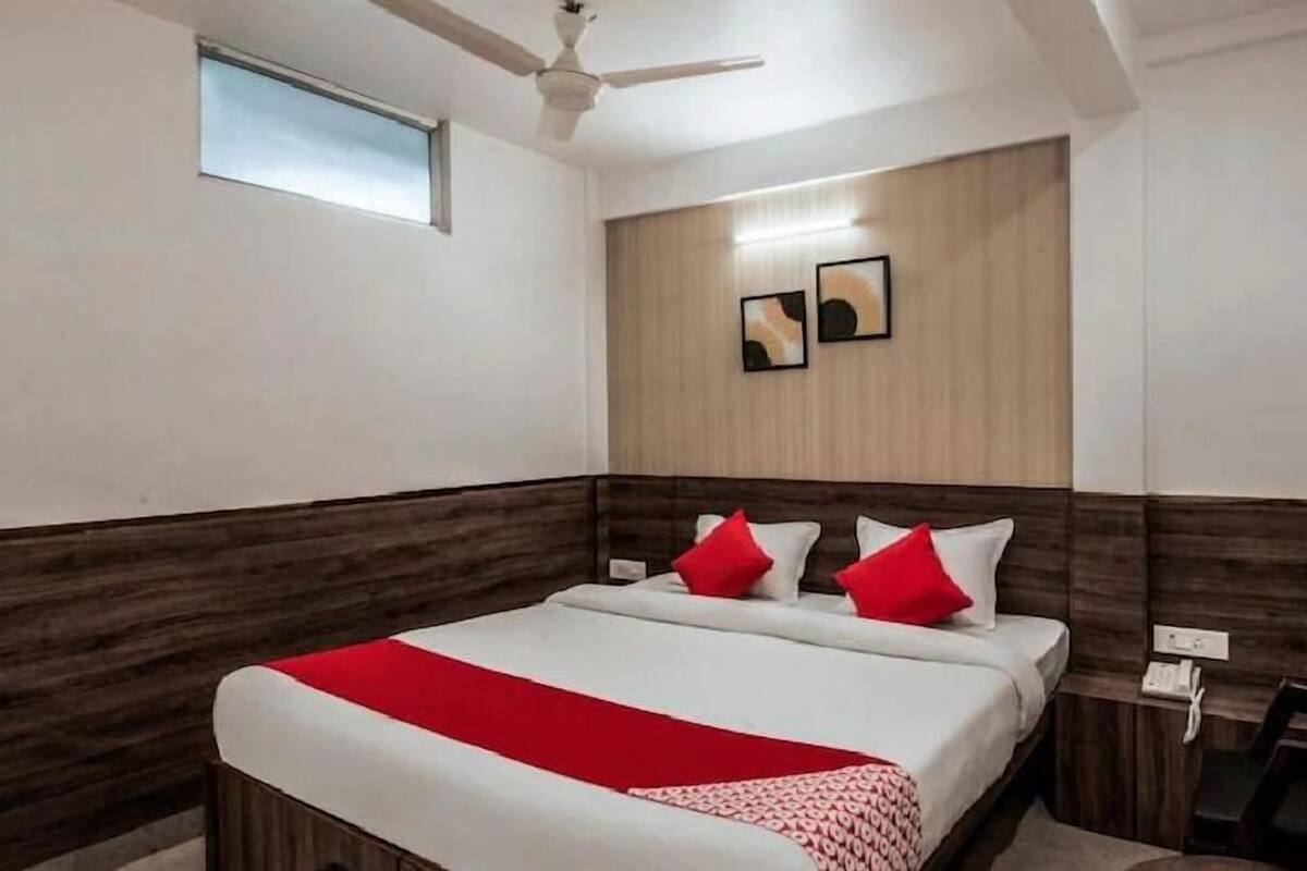 A hotel room with a bed, a ceiling fan, a bedside table with a phone, and a small window.