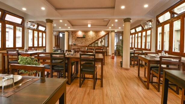 Ein geräumiges Restaurant mit Holztischen und -stühlen, großen Fenstern und einer Treppe, die in eine obere Ebene führt.