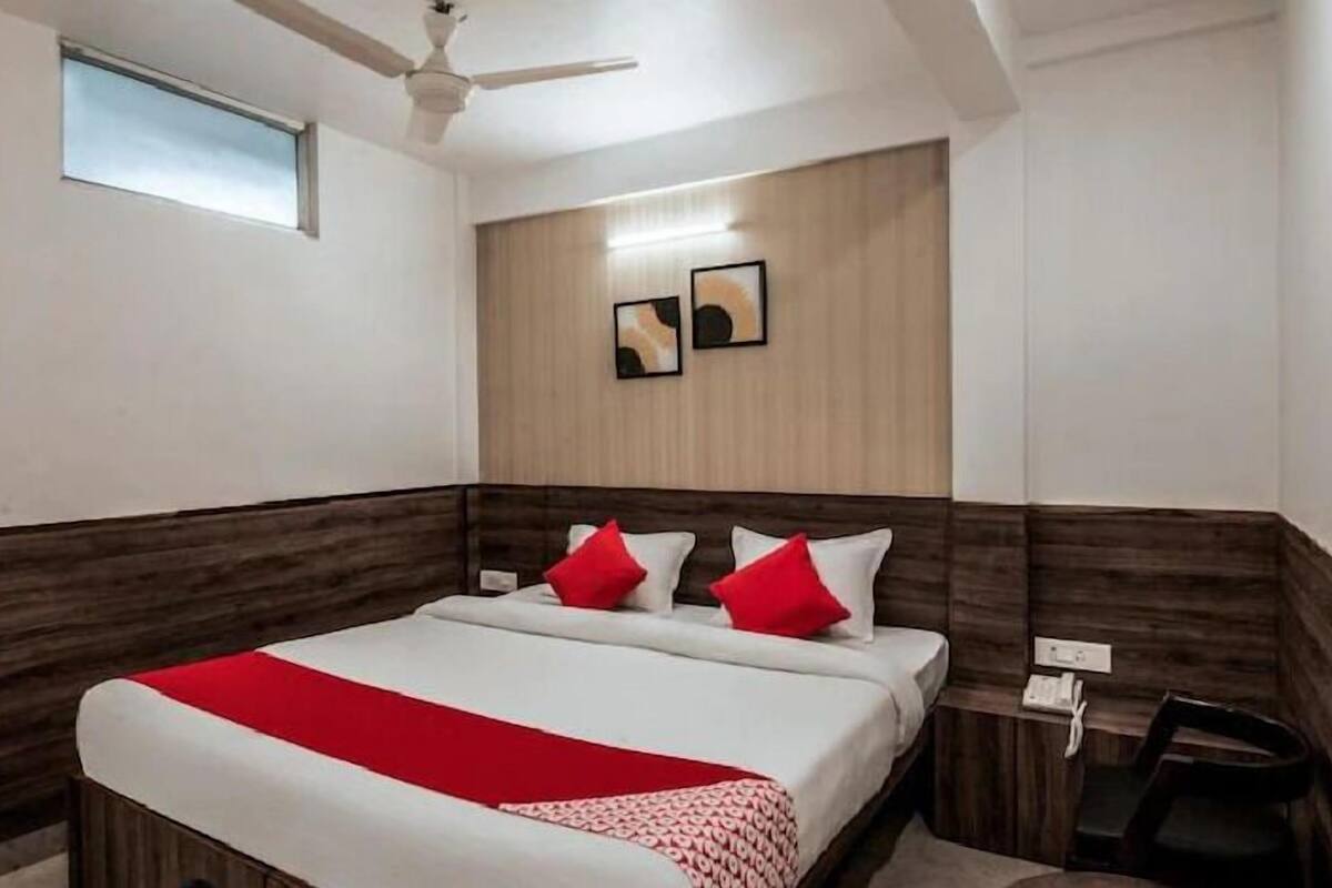 A hotel room with a bed, a ceiling fan, a small window, and a wooden accent wall.