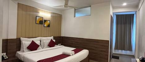 Una habitación de hotel con cama, escritorio, silla, ventilador de techo y ventana con cortinas.