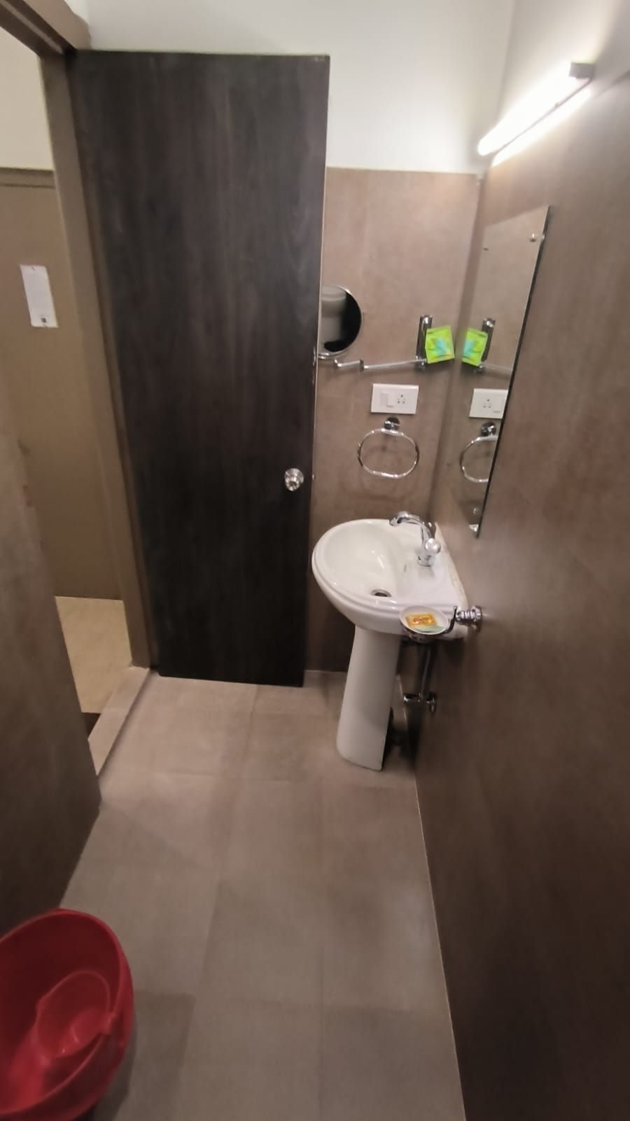 A bathroom with a white sink, a mirror, and a red bucket.