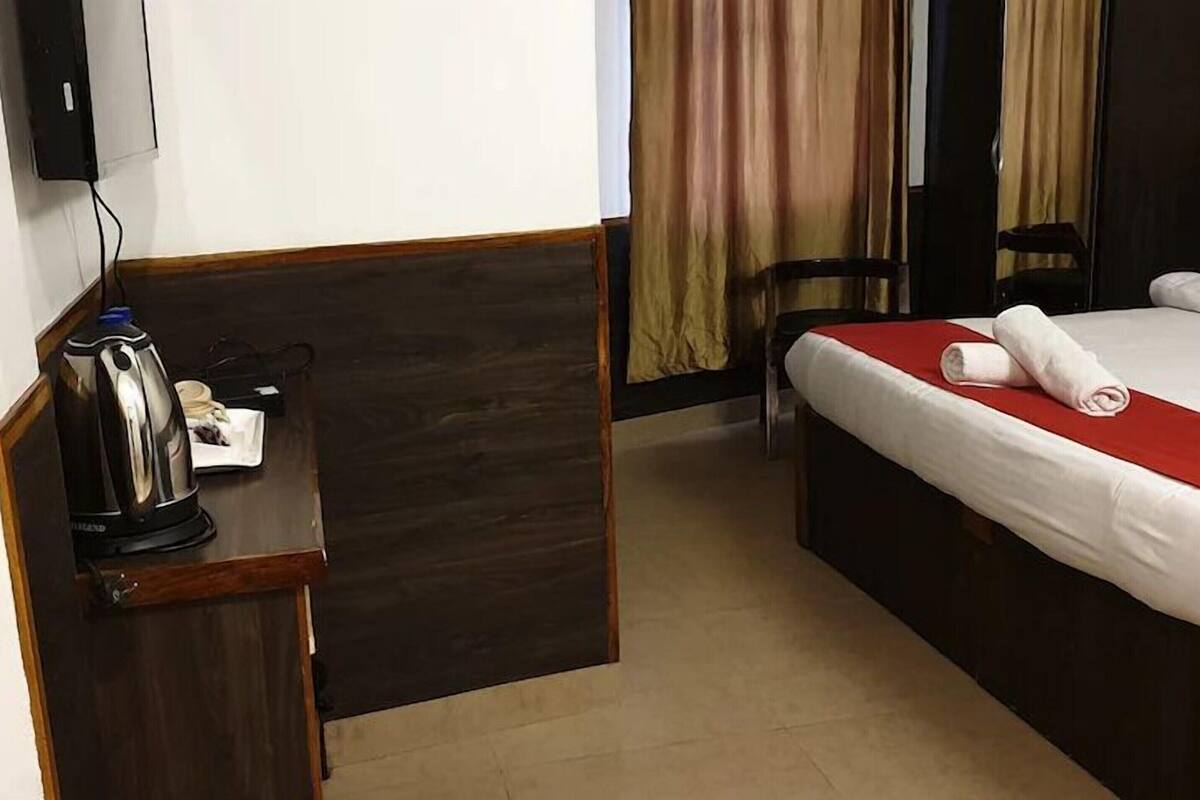 A hotel room with a bed, a desk with a kettle, and a chair.