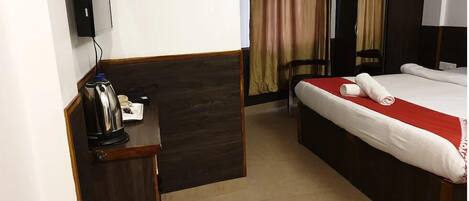 Una habitación de hotel con cama, escritorio con hervidor, silla y cortinas.