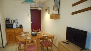 Een kleine keuken met houten kastjes, een magnetron, een waterkoker en een eettafel voor vier personen.