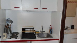 Een kleine keuken met witte kastjes, een spoelbak, een klein afdruiprek en een paar keukengerei.