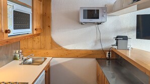 A compact kitchen with wooden cabinets, a built-in microwave, a sink, and a coffee machine. - Cozy ski-in studio with balcony (Les Arcs 1800)