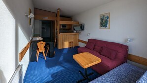 A compact room with a blue polka dot floor, a wooden table, a red sofa, a wooden bench, a microwave, and a television. - Cozy ski-in studio with balcony (Les Arcs 1800)
