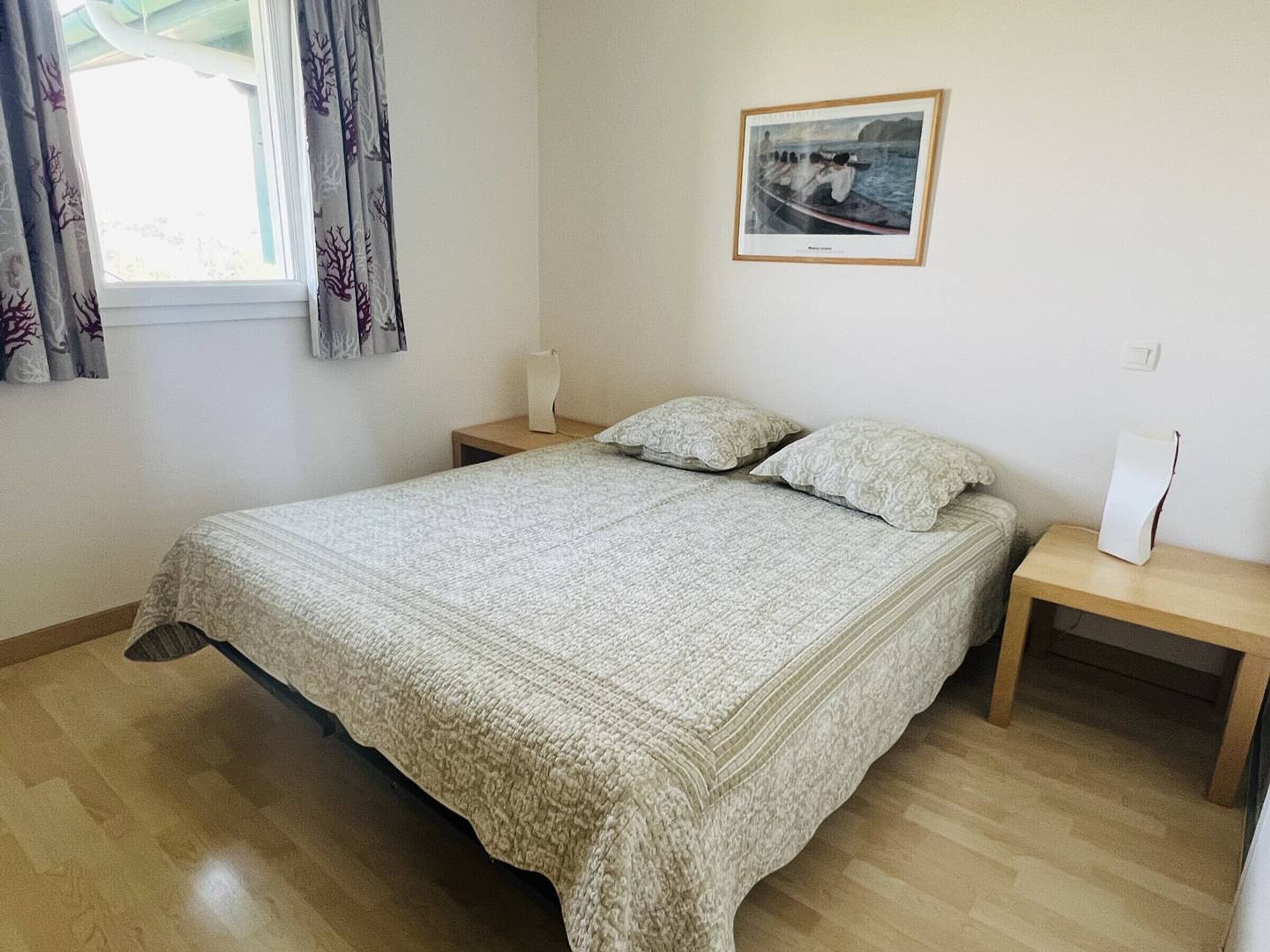 Ein Schlafzimmer mit einem großen Bett, zwei Nachttischen, einem Fenster mit Vorhängen und einem gerahmten Bild an der Wand.