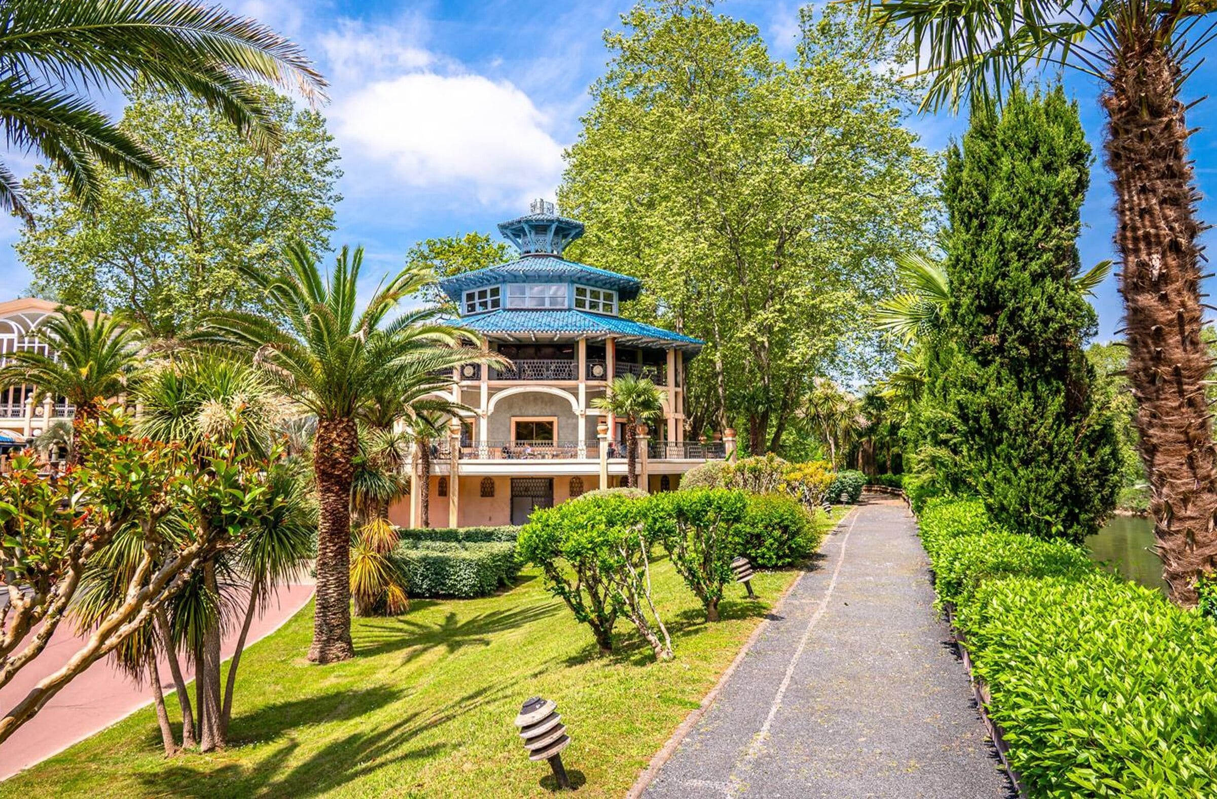 A traditional-style building with a blue roof, surrounded by lush greenery and palm trees.