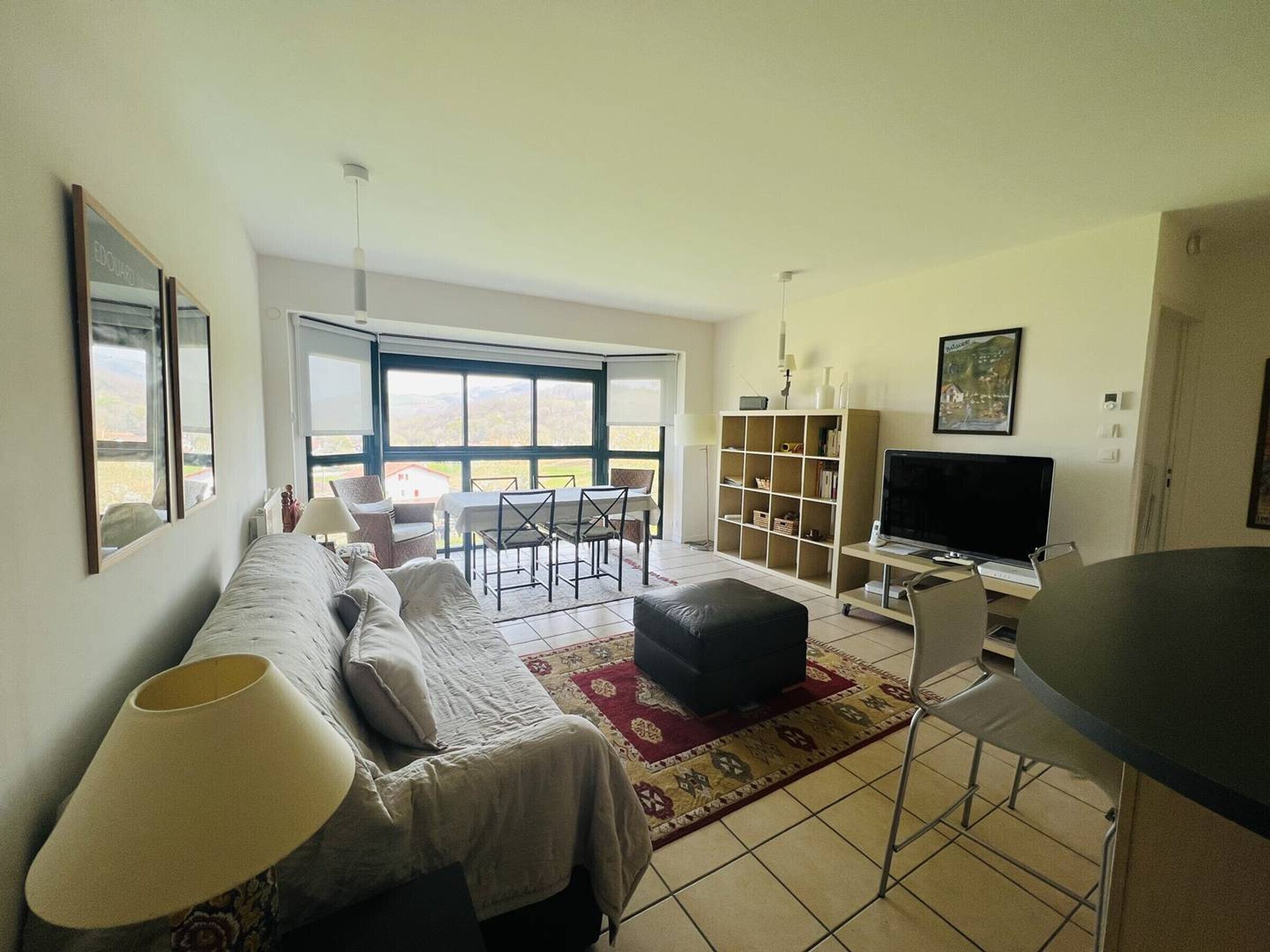 Ein Wohnzimmer mit Sofa, Fernseher, Bücherregal und Essbereich mit Stühlen und Tisch.