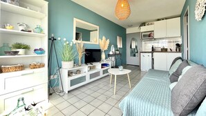 A modern living room with a sofa, a TV, and a dining area with a kitchen in the background. - 1-bedroom apartment with garage and pool in Sète (Sète)