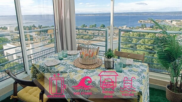 A balcony with a table set for dining, overlooking a cityscape and the sea. - 1-bedroom apartment with garage and pool in Sète (Sète)