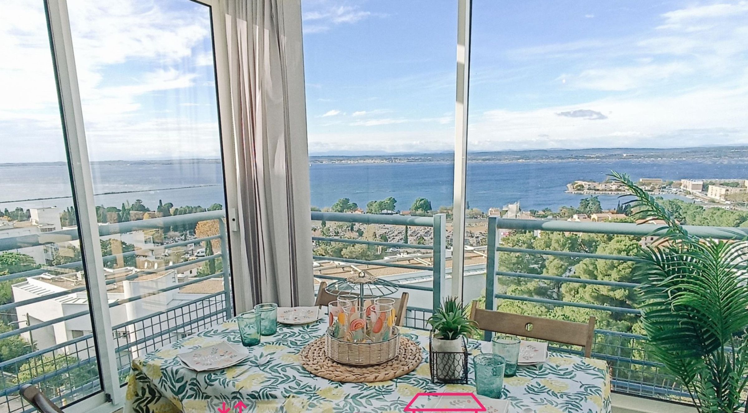 Un balcón con una mesa lista para comer, con vistas a la ciudad y al mar.
