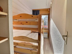 Une chambre avec un lit superposé, une fenêtre, une porte et une petite étagère.