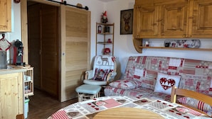 Una sala de estar acogedora con un sofá de madera, una mesa de comedor con colcha y una zona de cocina con armarios de madera y una máquina de café.