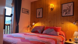Un dormitorio con pared de madera, cama con ropa de cama estampada, dos lámparas de pared y cuadros enmarcados.