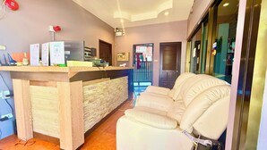 Un área de recepción con mostrador de madera, pared de piedra, sofá de cuero blanco y puerta que da al exterior.