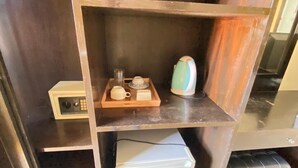 Una kitchenette compacta con microondas, hervidor de agua y una pequeña cafetera sobre una bandeja de madera.