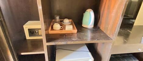 A compact kitchenette with a microwave, kettle, and a small coffee maker on a wooden tray.