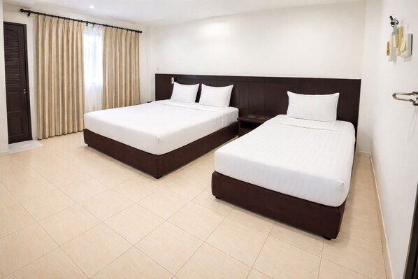 Habitación de hotel con dos camas individuales, cabecera oscura, cortinas color beige y suelo de baldosas.