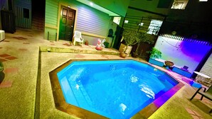 Una piscina con borde de madera, rodeada de una terraza de baldosas.