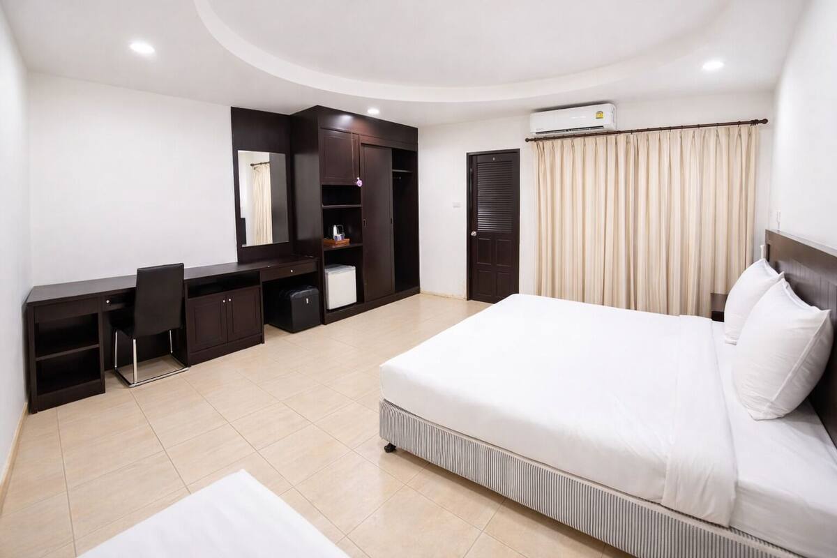 A modern hotel room with a bed, desk, chair, wardrobe, and an air conditioning unit.