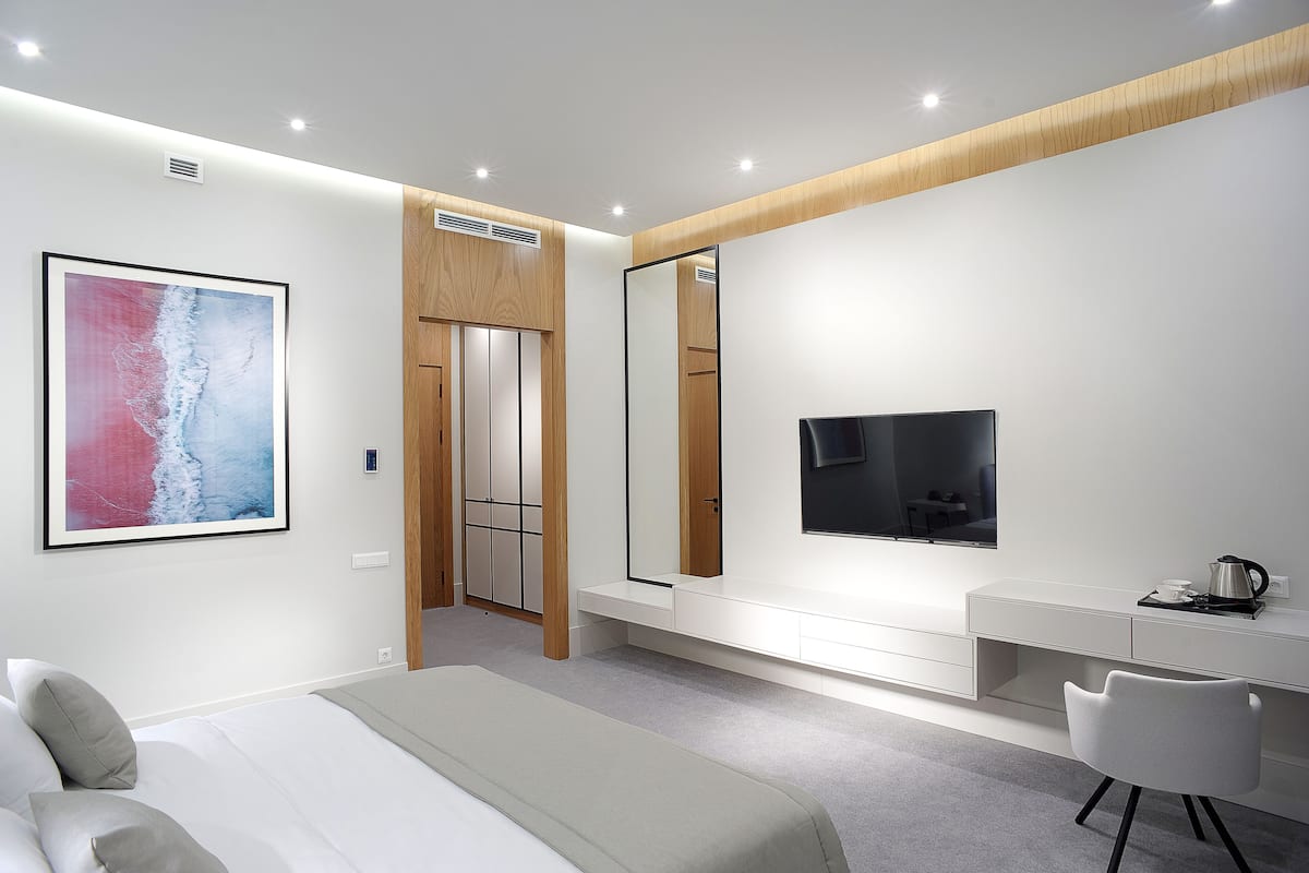 A modern bedroom with a bed, a desk, a chair, a TV, and a large mirror.
