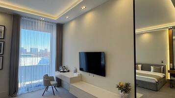 A modern hotel room with a large mirror, a flat-screen TV, a sofa, and a view of the city.