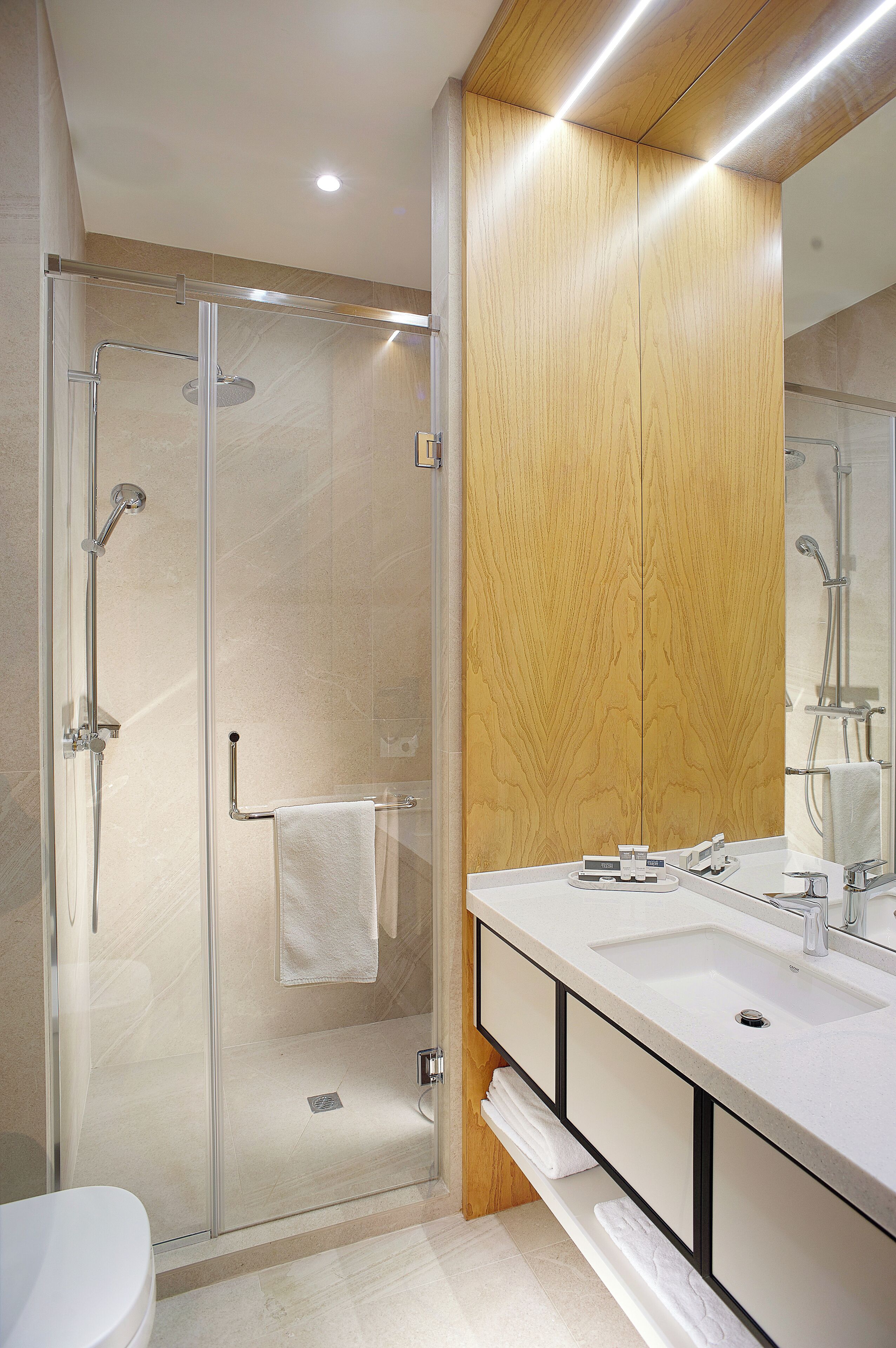 A modern bathroom with a glass-enclosed shower, a wooden vanity, and a large mirror.