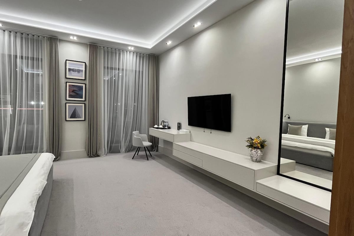 A modern hotel bedroom with a large bed, a desk, a TV, and a mirror.