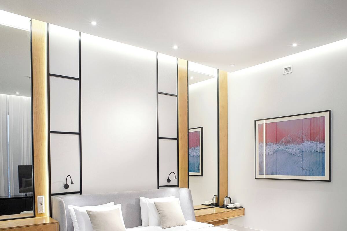 A modern bedroom with a bed, bedside tables, a bench, a TV, and artwork on the walls.