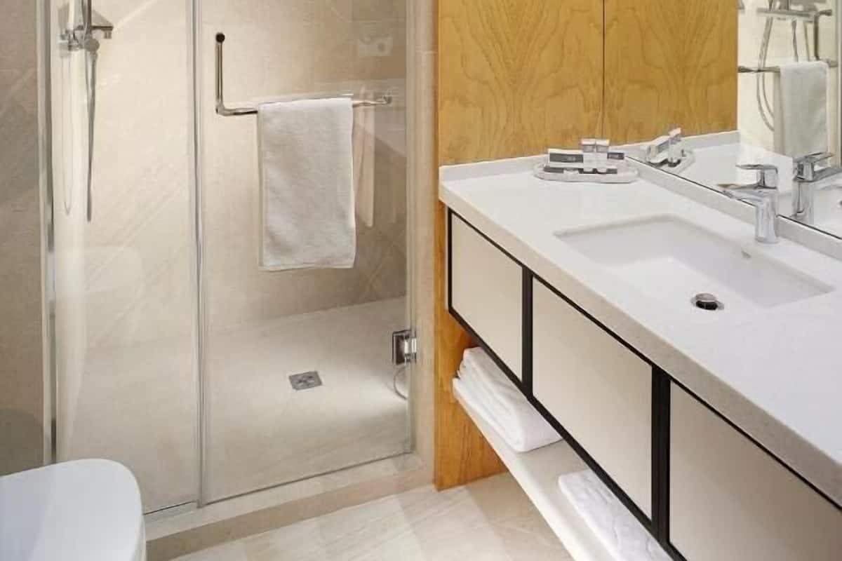 A modern bathroom with a glass-enclosed shower, a wooden vanity with a mirror, and a white sink.