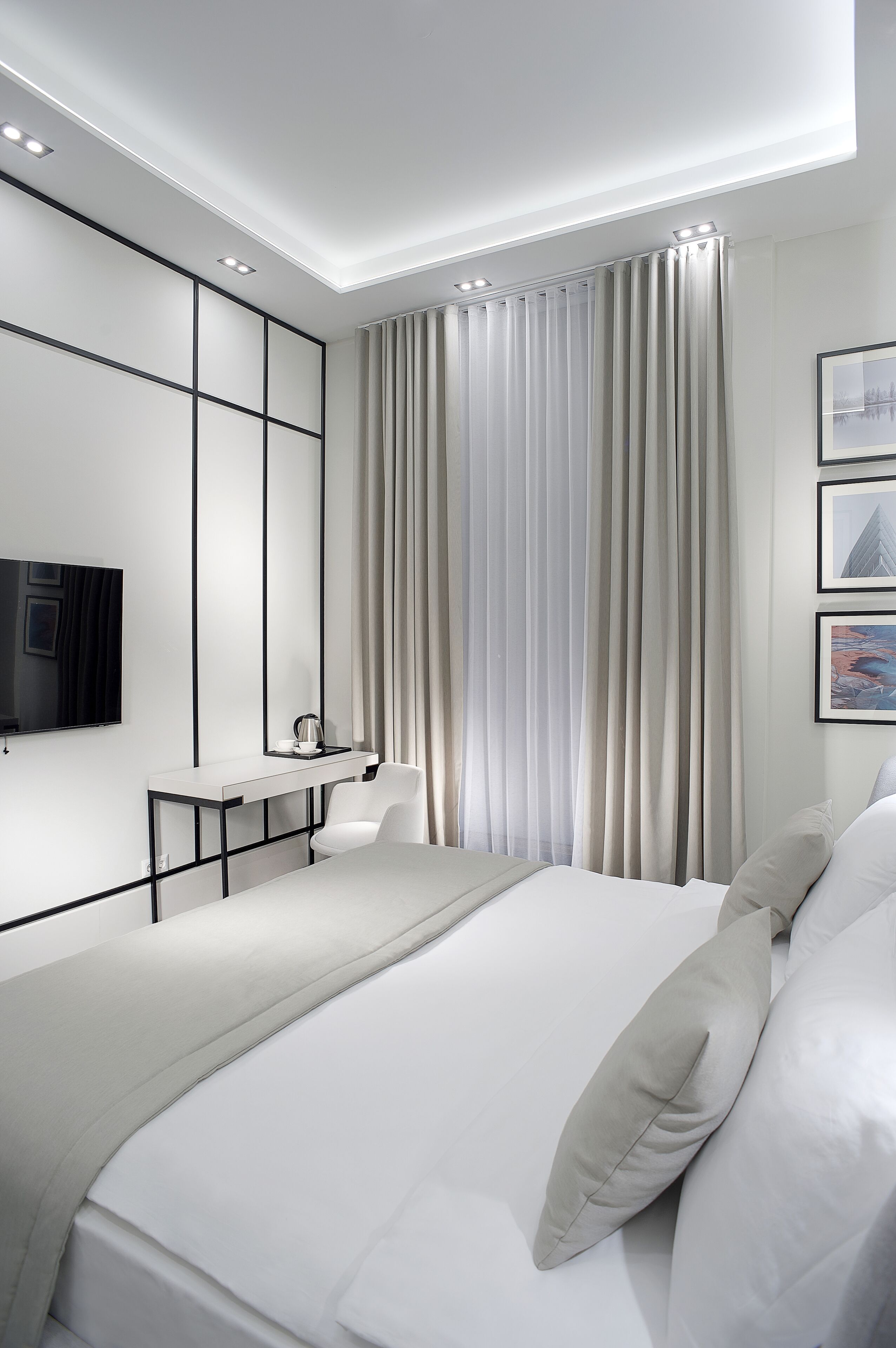A modern bedroom with a large bed, a bedside table, a TV mounted on the wall, and a window with curtains.
