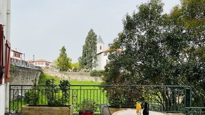 A patio with a round table and chairs, a potted plant, and a view of a church and buildings in the background. - Charming T2 apartment in Cambo, city center, small terrace, Internet, pets allowed (Cambo-les-Bains)