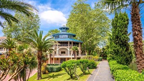 A traditional-style building with a blue roof, surrounded by lush greenery and palm trees. - Charming T2 apartment in Cambo, city center, small terrace, Internet, pets allowed (Cambo-les-Bains)