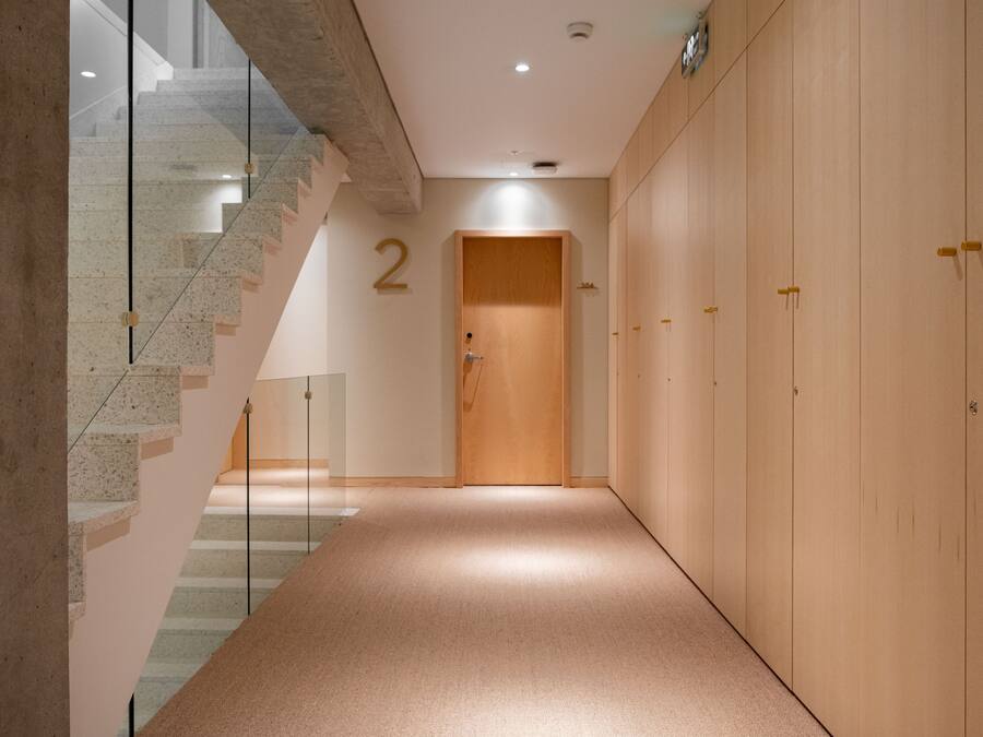 A hallway with a wooden door marked '2', a staircase with glass railings, and a carpeted floor.