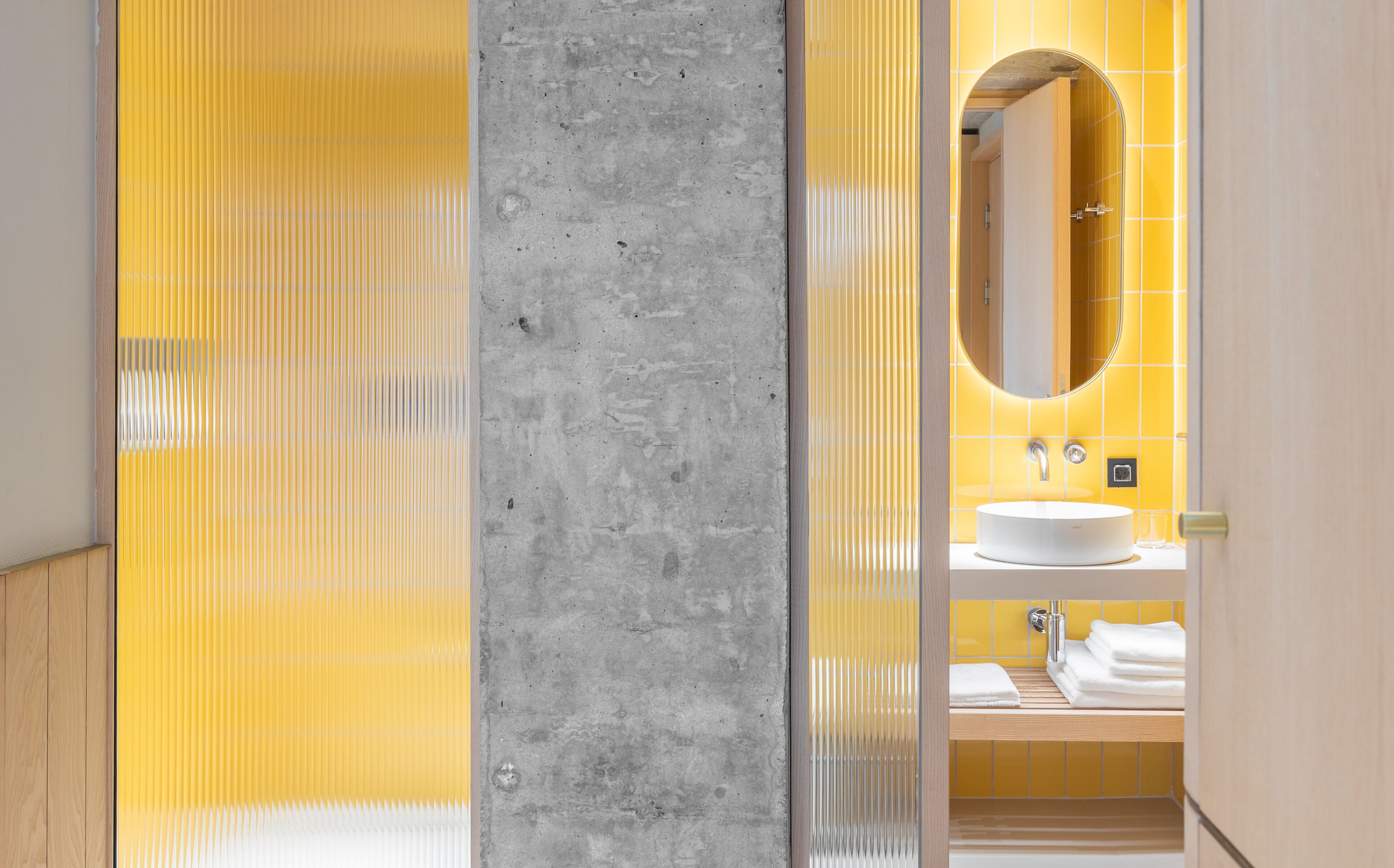 A modern bathroom with a concrete accent wall, a yellow tiled wall, and a white sink with a mirror above it.