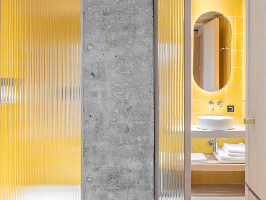 A modern bathroom with a concrete accent wall, a yellow tiled wall, and a white sink with a mirror above it.