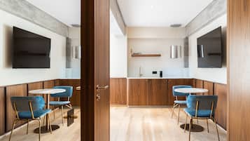 A modern dining area with wooden paneling, a kitchen counter, and two TVs mounted on the walls.