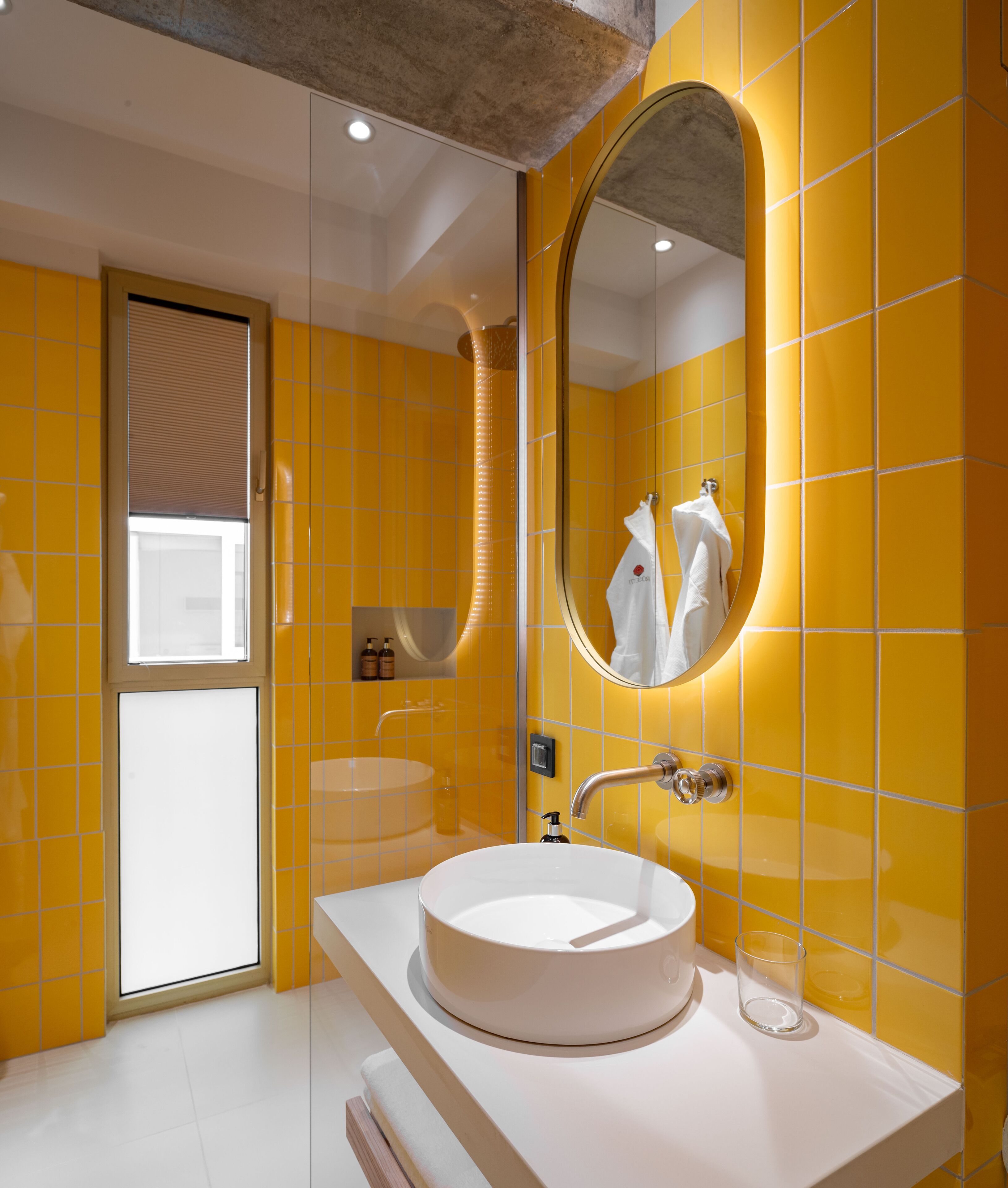 Un baño moderno con paredes de azulejos amarillos, un lavabo blanco y un espejo grande.