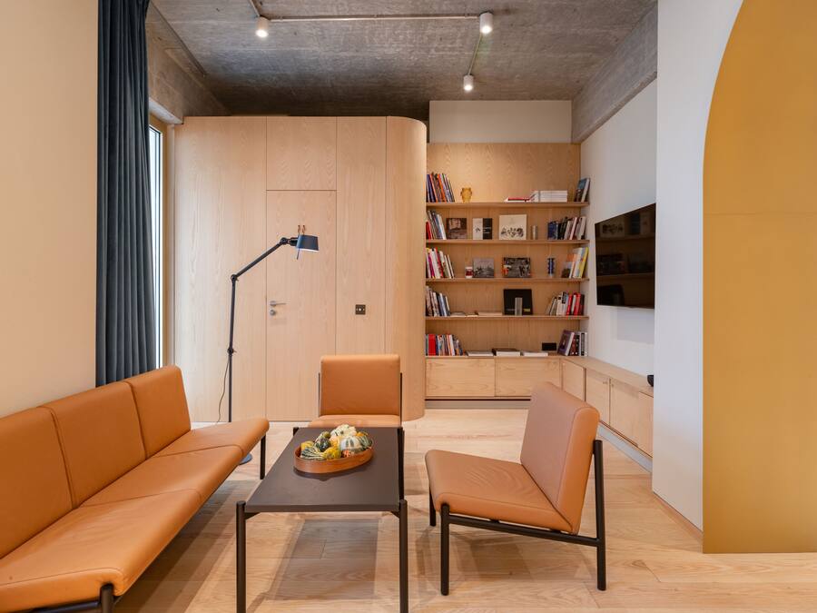 Una sala moderna con sofá, sillón y una mesa de centro, una estantería llena de libros y un televisor de pantalla plana montado en la pared.