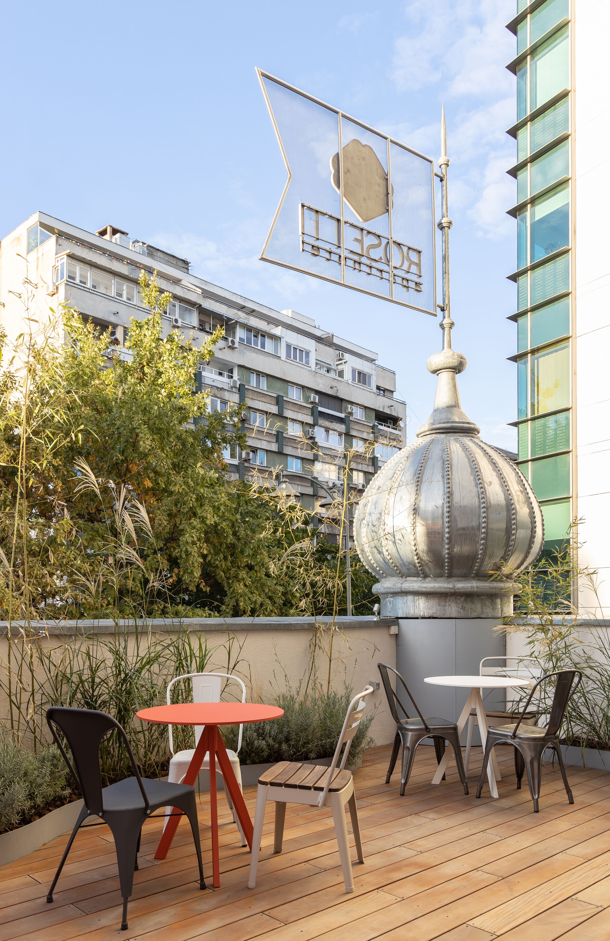 Una terrazza sul tetto con una sfera di metallo decorativa, un tavolo con sedie e vista su un edificio moderno sullo sfondo.