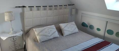 Un dormitorio con cama, mesita de noche, lámpara y ventana.