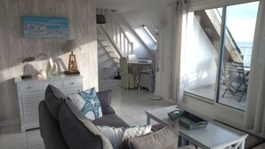 En stue med sofa, sofabord og havudsigt gennem store vinduer.
